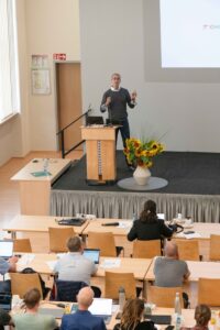 Photo of a man (Josh Moore) giving a presentation in front of an audience.